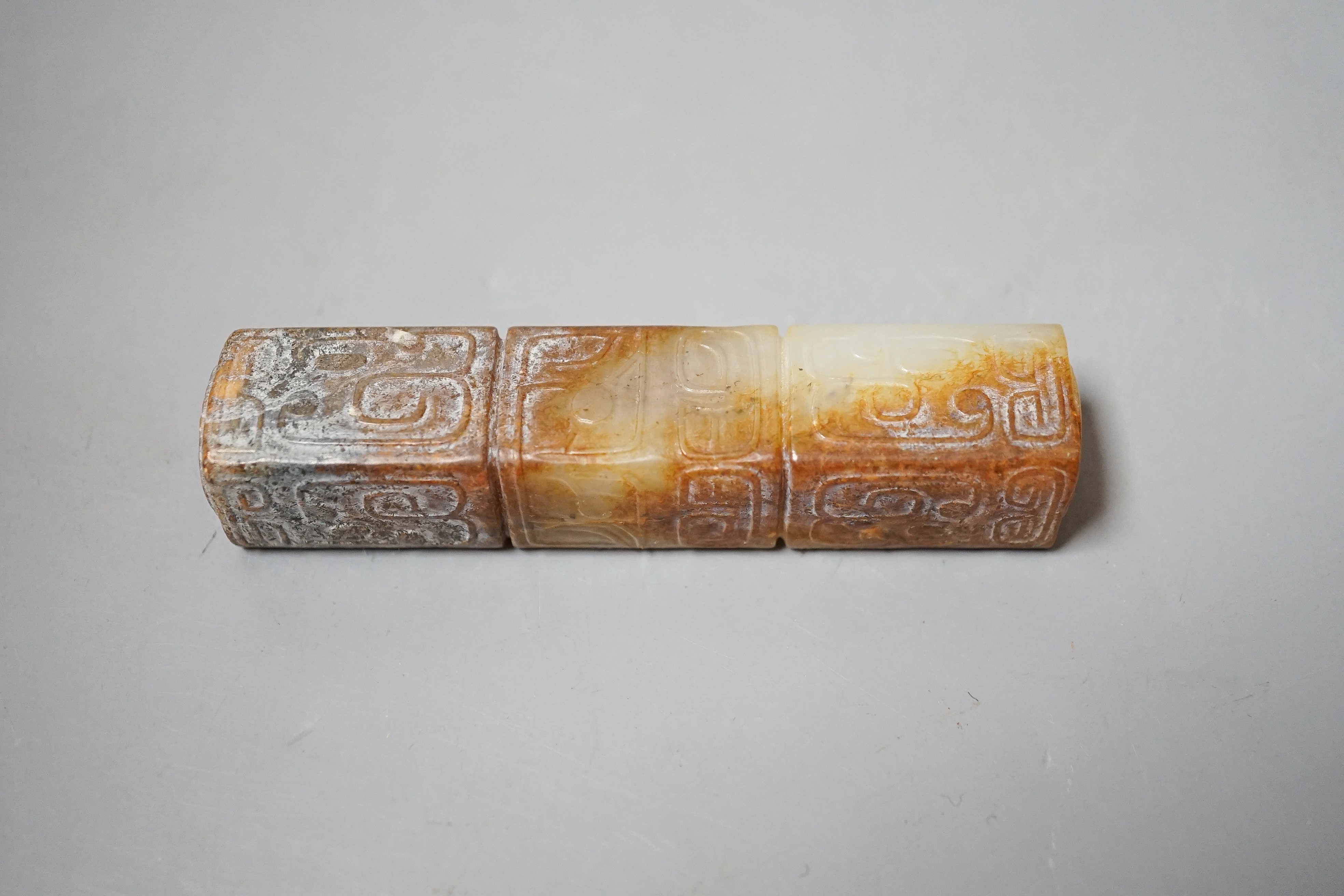 A Chinese archaistic white and russet jade handle mount, carved in relief with three registers of taotie masks, height 9.7cm